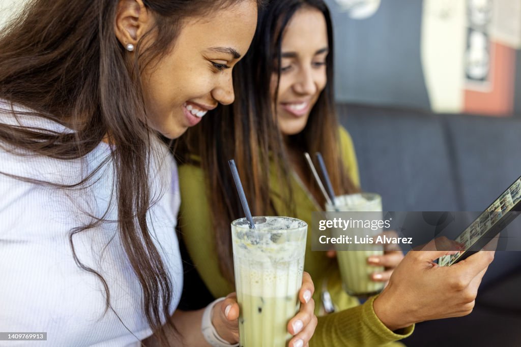 Women friends using phone and drinking iced matcha latte at a cafe