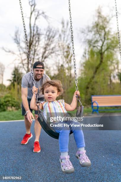 verspielter vater, der tochter auf schaukel im park schiebt - schaukel stock-fotos und bilder