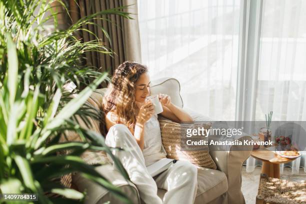 woman at home reading book and drinking coffee. - voertuiginterieur stockfoto's en -beelden