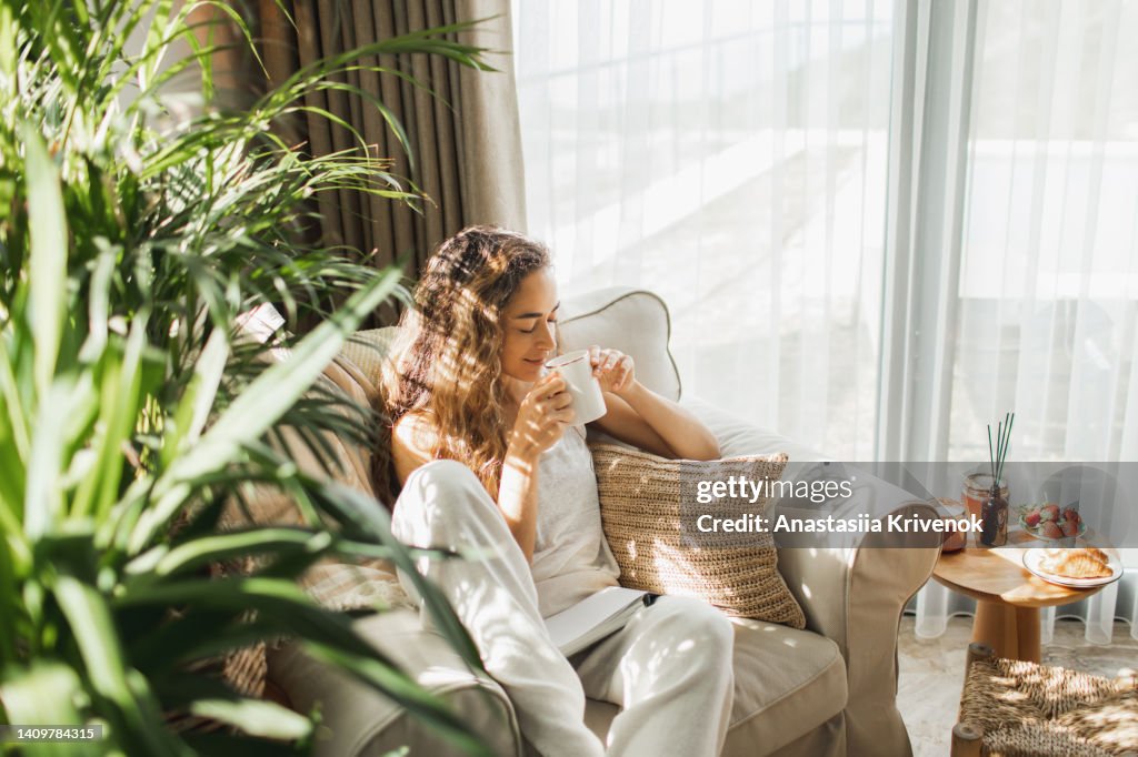 Woman at home reading book and drinking coffee.