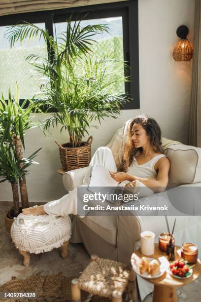 woman at home reading book and drinking coffee. - wohngebäude innenansicht stock-fotos und bilder
