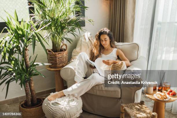 woman at home reading book and drinking coffee. - wohngebäude innenansicht stock-fotos und bilder