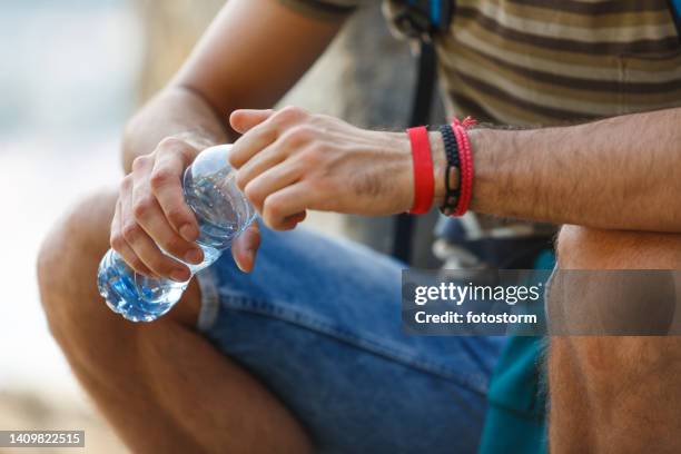 man relaxing on the city street, opening a bottle of water to hydrate after a hike - drinking from bottle stock pictures, royalty-free photos & images