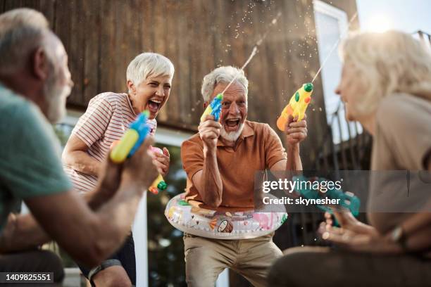 felices parejas mayores divirtiéndose durante la pelea de armas de agua en una terraza. - man splashed with colour fotografías e imágenes de stock