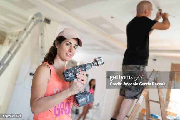 woman covered with remains of construction dust looks. camera smiling with drill and bit while working on home renovation - drill bit stockfoto's en -beelden