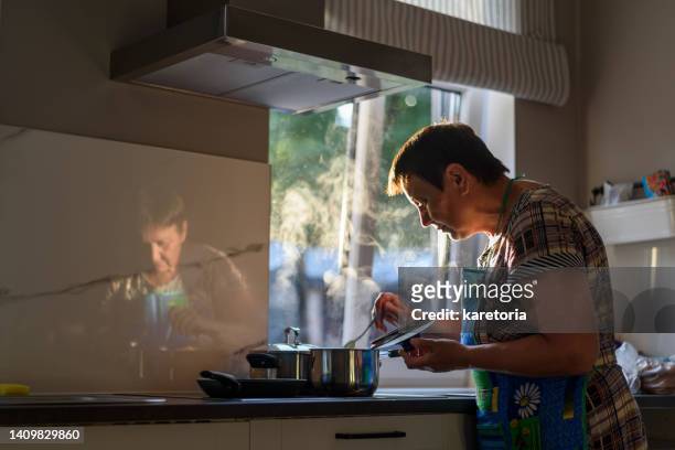 mature woman cooking near window - one person standing stock pictures, royalty-free photos & images