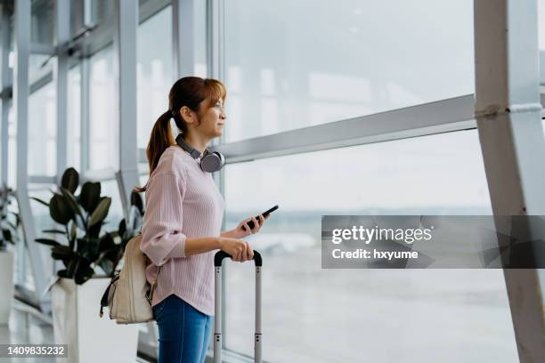 asian woman tourist using smartphone in airport terminal - woman airplane headphones bildbanksfoton och bilder