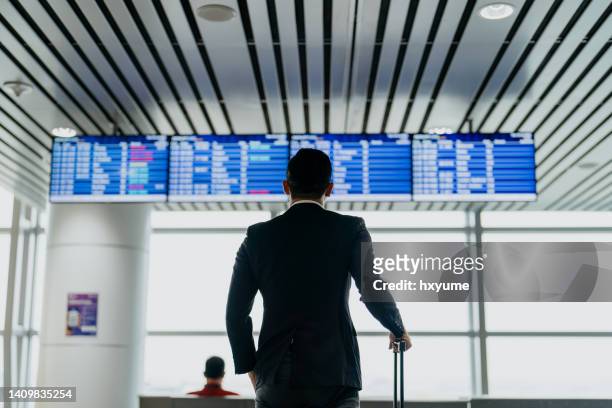 asiatischer geschäftsmann schaut auf ankunftsabflugtafel im flughafenterminal - kuala lumpur airport stock-fotos und bilder