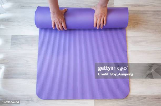 high angle view of woman hands folding purple yoga or fitness mat after working out at home. - mat stock pictures, royalty-free photos & images