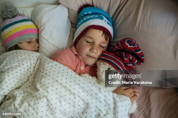 children sleeping in their bed wearing winter hats - cold temperature inside stock pictures, royalty-free photos & images