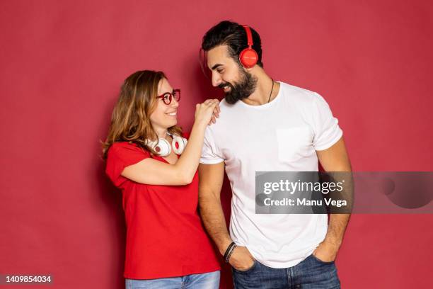 smiling couple using wireless headphones while standing over an isolated red background. - headphones isolated ストックフォトと画像