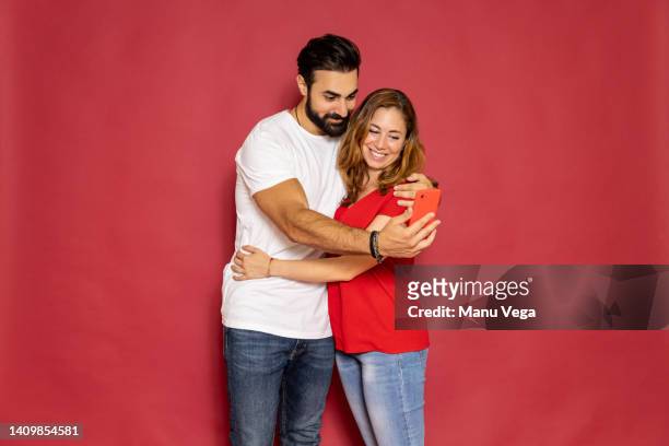 smiling couple taking a selfie with a mobile phone over an isolated red background. - middle eastern male on phone isolated stock pictures, royalty-free photos & images