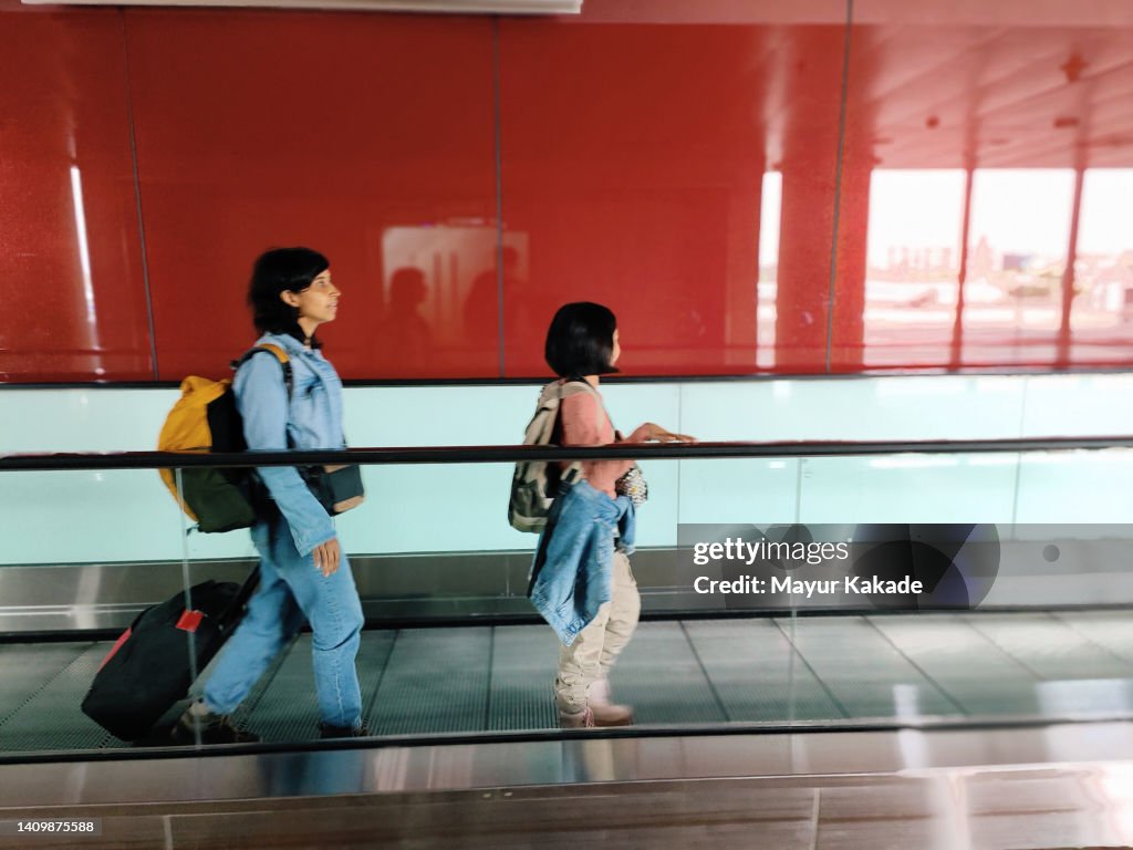 Mother and daughter on a moving walkway at the airport carrying their luggage
