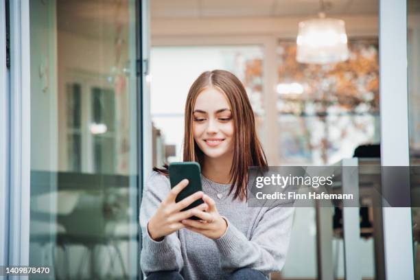 lächelnde frau, die auf der treppe sitzt und nachrichten auf dem handy liest - online dating stock-fotos und bilder