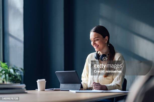 happy female student studying online on a digital tablet - looking over laptop stock pictures, royalty-free photos & images