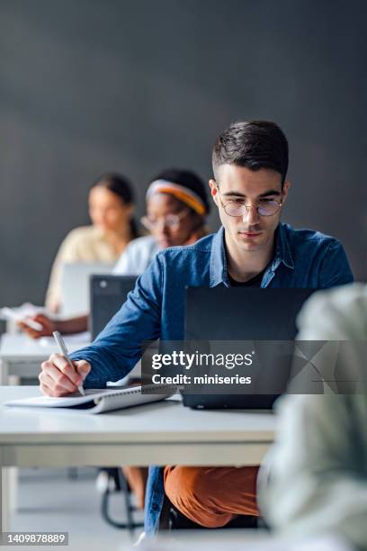 universitätsstudenten machen sich notizen, während sie im klassenzimmer sitzen - schulische prüfung stock-fotos und bilder