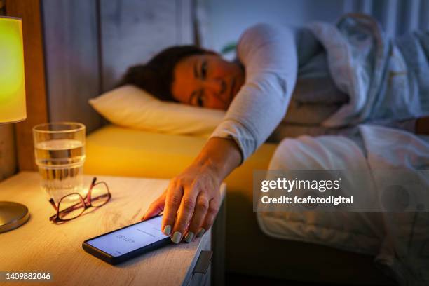 frau im bett greift auf nachttisch zum handy - sleep female handphone stock-fotos und bilder