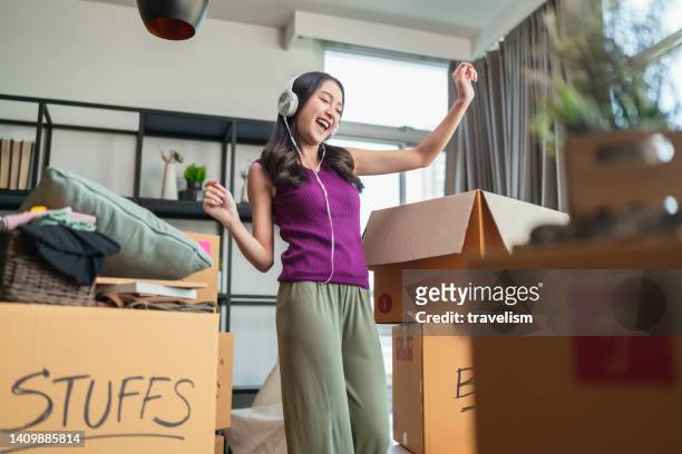 ้幸福 アジアの女性 大人の女性 陽気なダンスの動きと箱から物を開梱 リラックス カジュアルにヘッドフォンを身に着けながら 新しい家、家の家のアパート ブームのアイデアの概念 - 賃借人 ストックフォトと画像