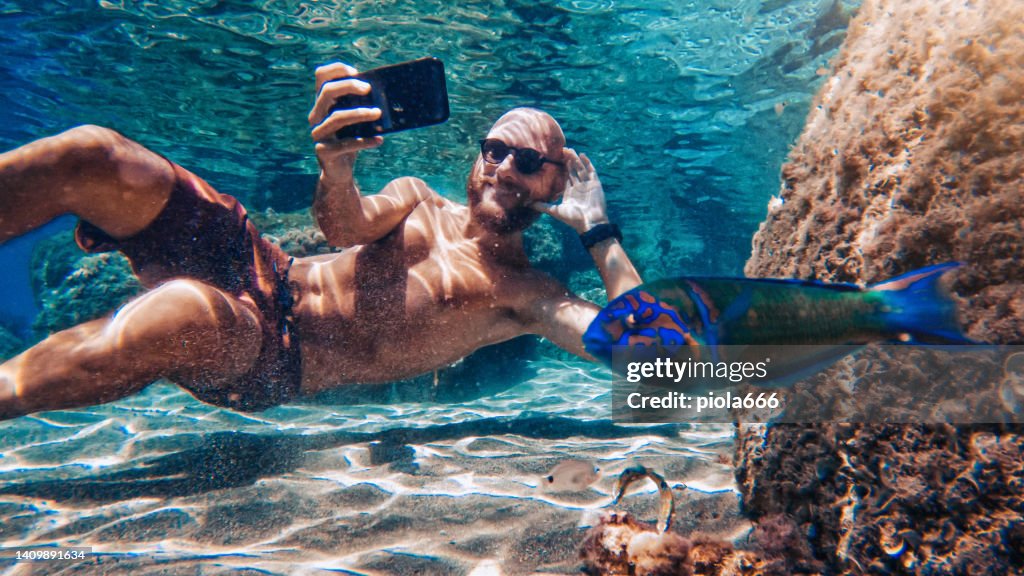 Selfie avec téléphone portable sous l’eau en mer: photobombardage de poissons