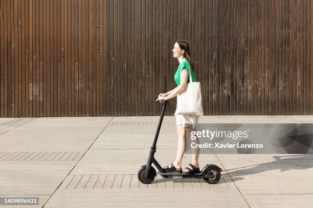 smiling young woman riding an electric scooter outdoors. - scooter stockfoto's en -beelden