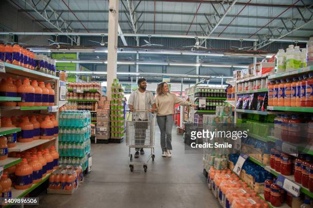 couple pushing empty trolley in supermarket - mercado espaço de venda no varejo - fotografias e filmes do acervo