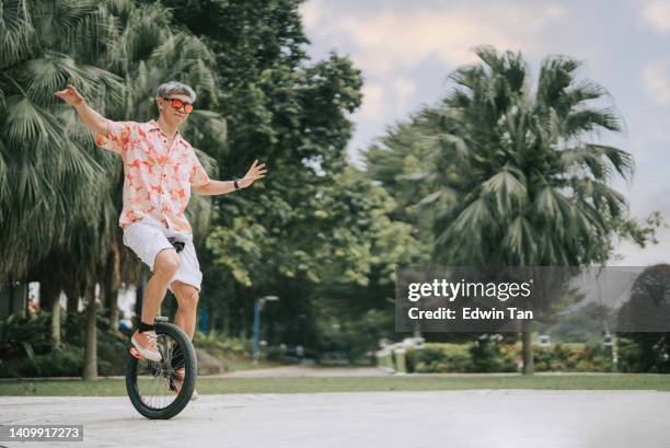 asian chinese mature man practising unicycle at public park - unicycle stock pictures, royalty-free photos & images