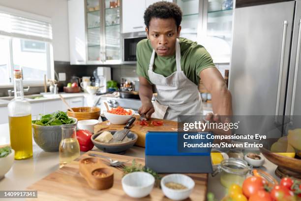 young man preparing healthy meal with online recipe in kitchen - kitchen apron stock pictures, royalty-free photos & images