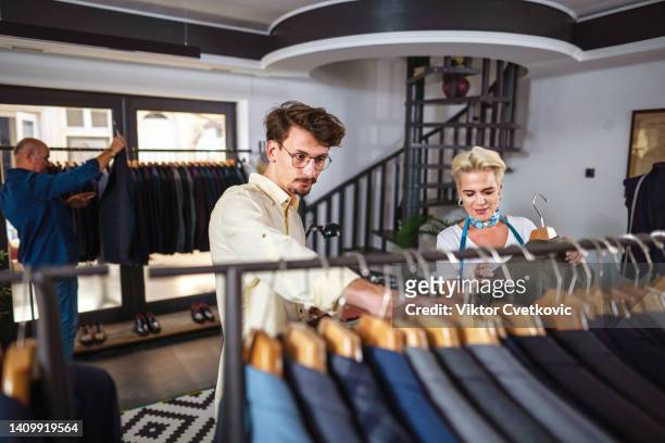 operaia che mostra abiti da cliente maschile nel negozio - abbigliamento da uomo foto e immagini stock