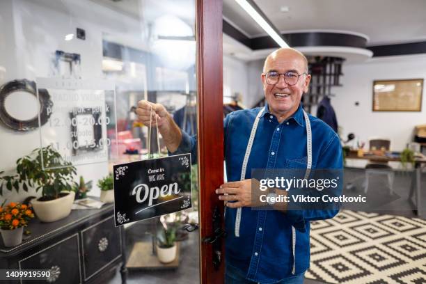 senior male tailor opening the door at men's clothing store - custom tailored suit stock pictures, royalty-free photos & images