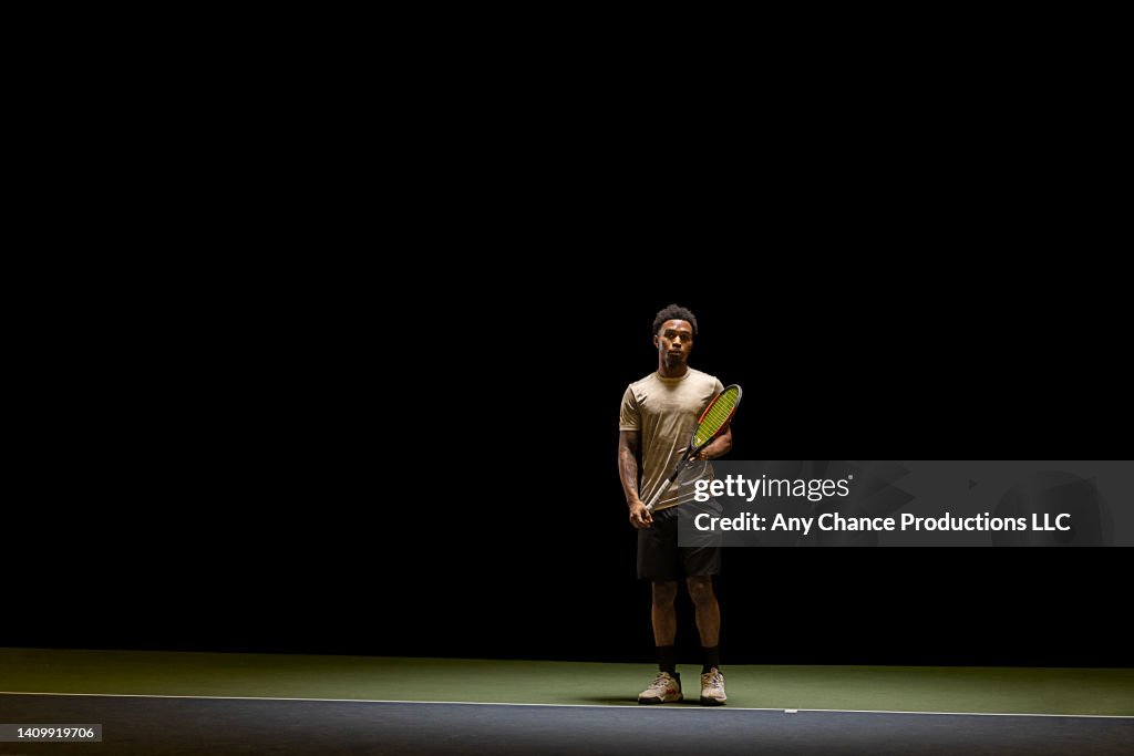 Tennis player at the back of the court looks on before playing.