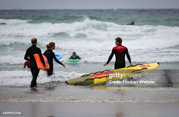 Lifeguard, carrying a rescue board, directs bodyboarders to surf between the red and yellow flags in the sea at Polzeath beach, on July 20, 2022 in...