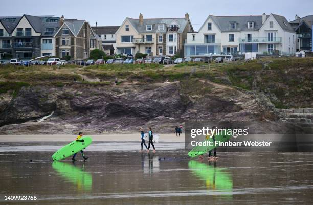 People leave the sea carrying their surfboards at Polzeath beach, on July 20, 2022 in Polzeath, United Kingdom.