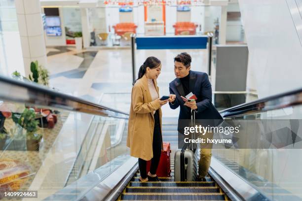 zwei asiatische geschäftsreisende fahren auf einer rolltreppe im flughafen - kuala lumpur airport stock-fotos und bilder