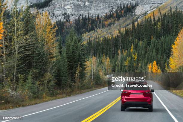 a red crossover car driving fast on the countryside asphalt road against blue sky with white clouds. a long straight road leading towards a snow capped mountain in new zealand - wonderlust stock-fotos und bilder