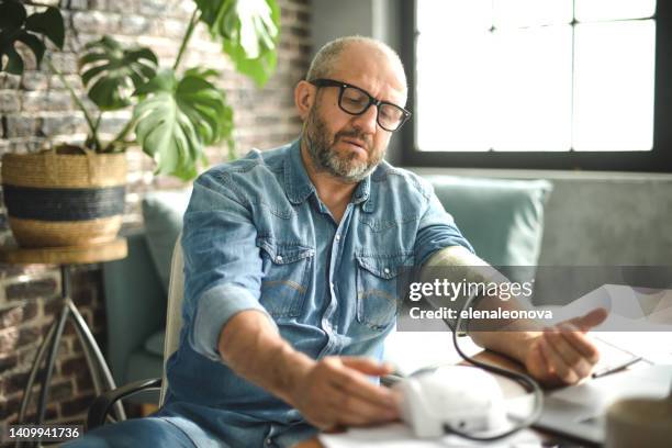 reifer erwachsener mann, der vom büro aus arbeitet (mit einer klassischen tonometermessung) - messgerät stock-fotos und bilder