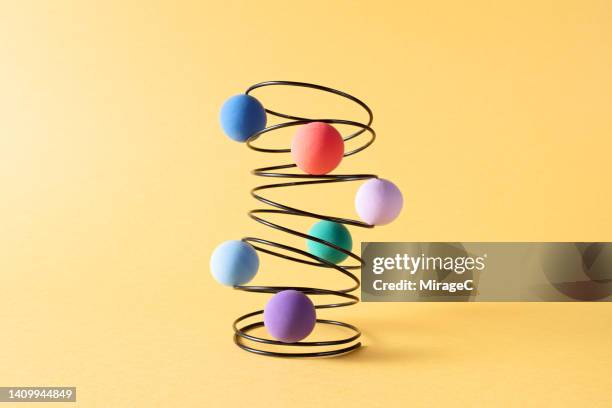 colorful spheres embedded in a swirl-shaped coil spring - physical pressure stock pictures, royalty-free photos & images