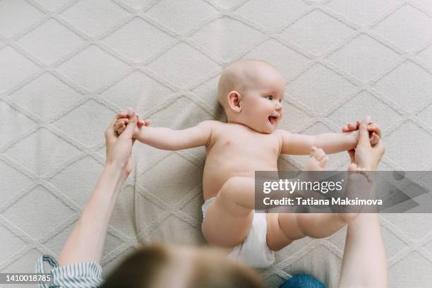 cute nude baby is lying on a light beige blanket at home. mom does gymnastics with a baby. - baby eltern von oben stock-fotos und bilder