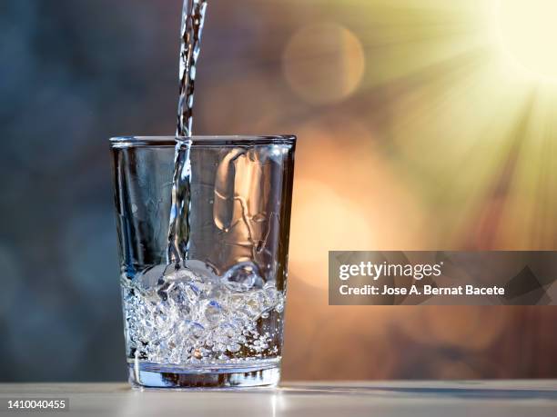 filling a glass of water to drink illuminated by sunlight. - wasserglas stock-fotos und bilder