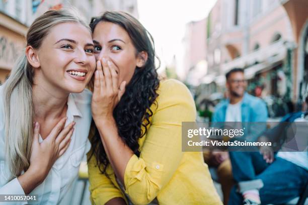 zwei junge freundinnen sitzen im stadtcafé und tratschen. - whispering stock-fotos und bilder