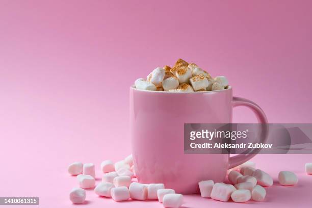 a cup of hot cocoa or coffee with marshmallows sprinkled with cinnamon spices on a bright pastel pink background. small airy meringues are scattered nearby. the concept of food and unhealthy eating. copy space. - excess sugar stock pictures, royalty-free photos & images