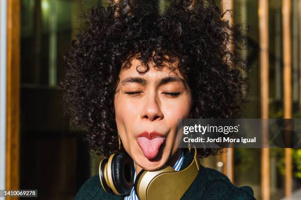 woman sticking the tongue out outdoors - grimassen stock-fotos und bilder