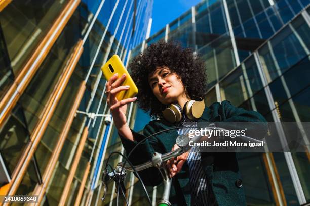 low angle view of a woman using a mobile while leaning on a bike outdoors - ver fotografías e imágenes de stock