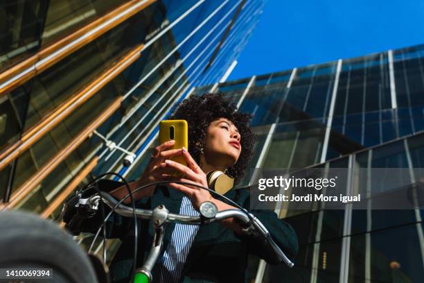 beauty woman in a bike using a mobile with distracted look - mobile phone reading low angle stock pictures, royalty-free photos & images