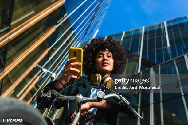 beauty woman looking at camera while using a mobile and sitting on a bike - elektro fahrrad stock-fotos und bilder