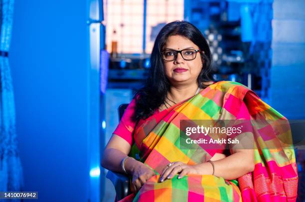 portrait of a happy woman of indian ethnicity wearing traditional dress sari and sitting on sofa at home. - indian wedding dress stock pictures, royalty-free photos & images