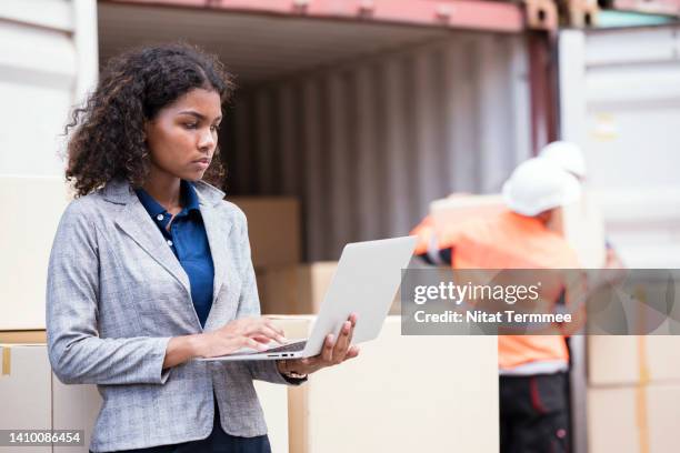 pre-loading and visual inspection of cargo containers. an african american female supervisor is inspecting stock while using a laptop to verify of labeling and quality of cargo packaging. - funcionário de alfândega imagens e fotografias de stock