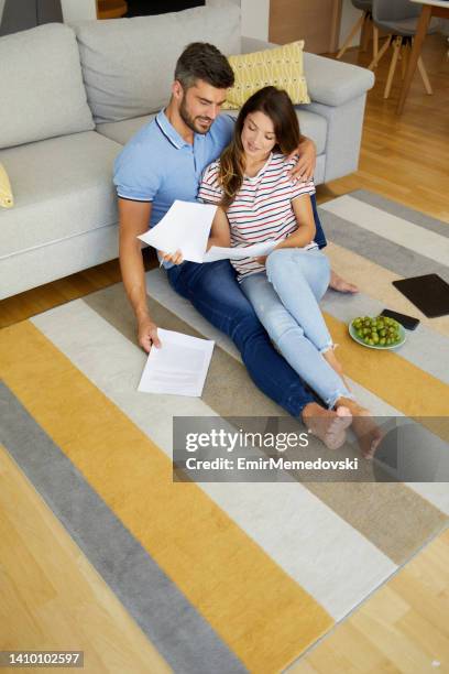 mid adult couple sitting together on carpet in living room and checking their finances - demonstration against the marriage for all bill stock pictures, royalty-free photos & images