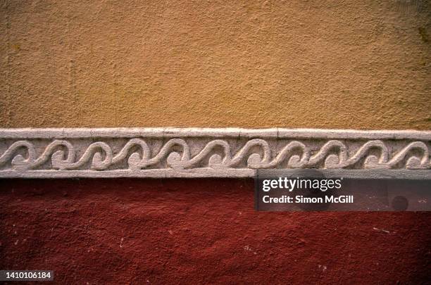 colonial building exterior wall painted yellow and rusty red with a decorative white band with a crashing wave relief pattern - bump band stock pictures, royalty-free photos & images
