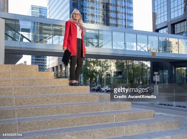 senior female business executive ascends concrete staircase, business district behind - calgary bridge stock pictures, royalty-free photos & images