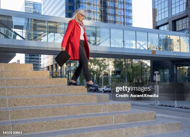 senior female business executive ascends concrete staircase, business district behind - woman walks down street stock pictures, royalty-free photos & images